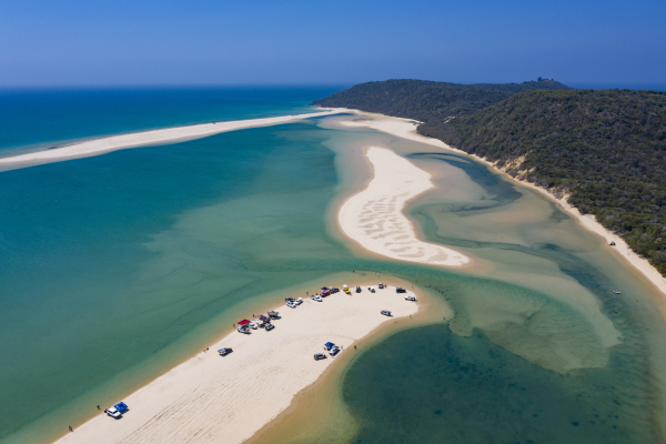 an aerial view of a sandspit with cars on the beacg