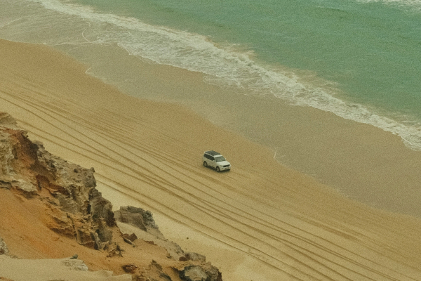 an aerial view of a car driving along a beach with the ocean in the background
