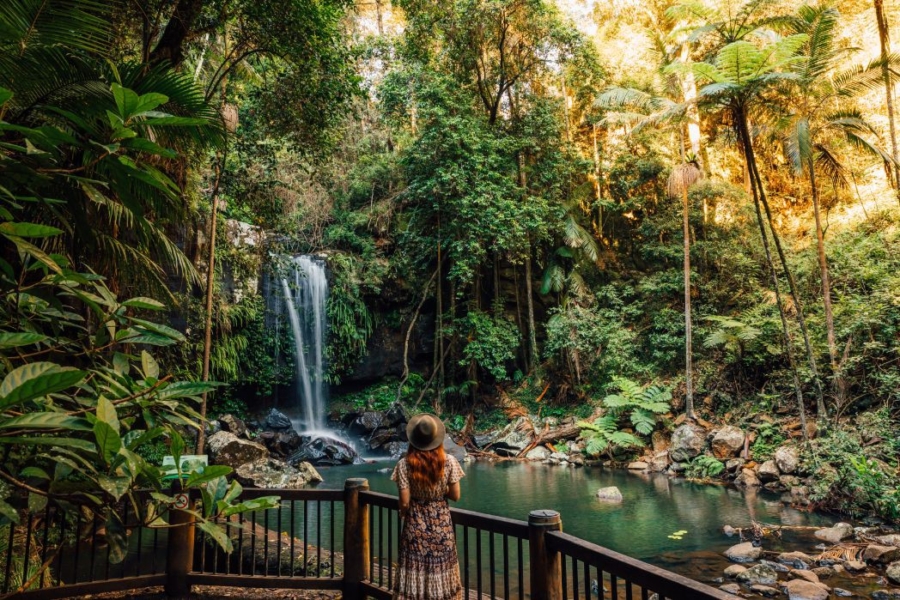 A redheaded woman with a hat at an observation viewing area in front of a small waterfall