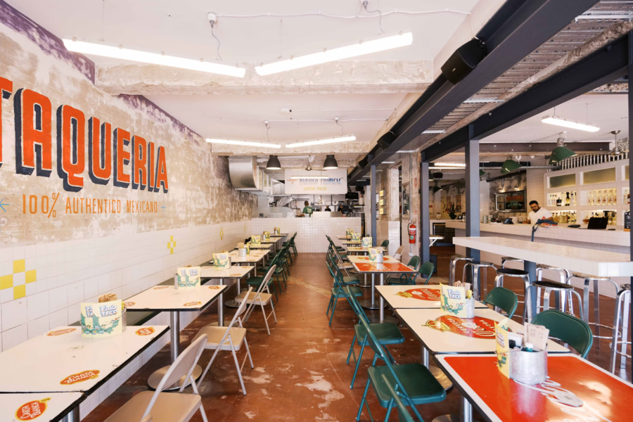 An interior shot of a taco bar with two rows of tables and a mexican theme. There is a bar in the background